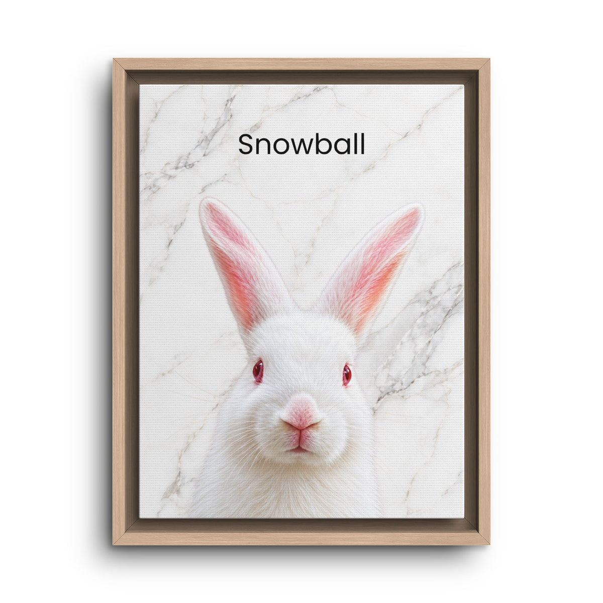 A framed art print featuring a white rabbit with pink inner ears and red eyes on a white marble background, with the text 'Snowball' at the top. The print is housed in a light natural wood frame and is shown against a plain white background.