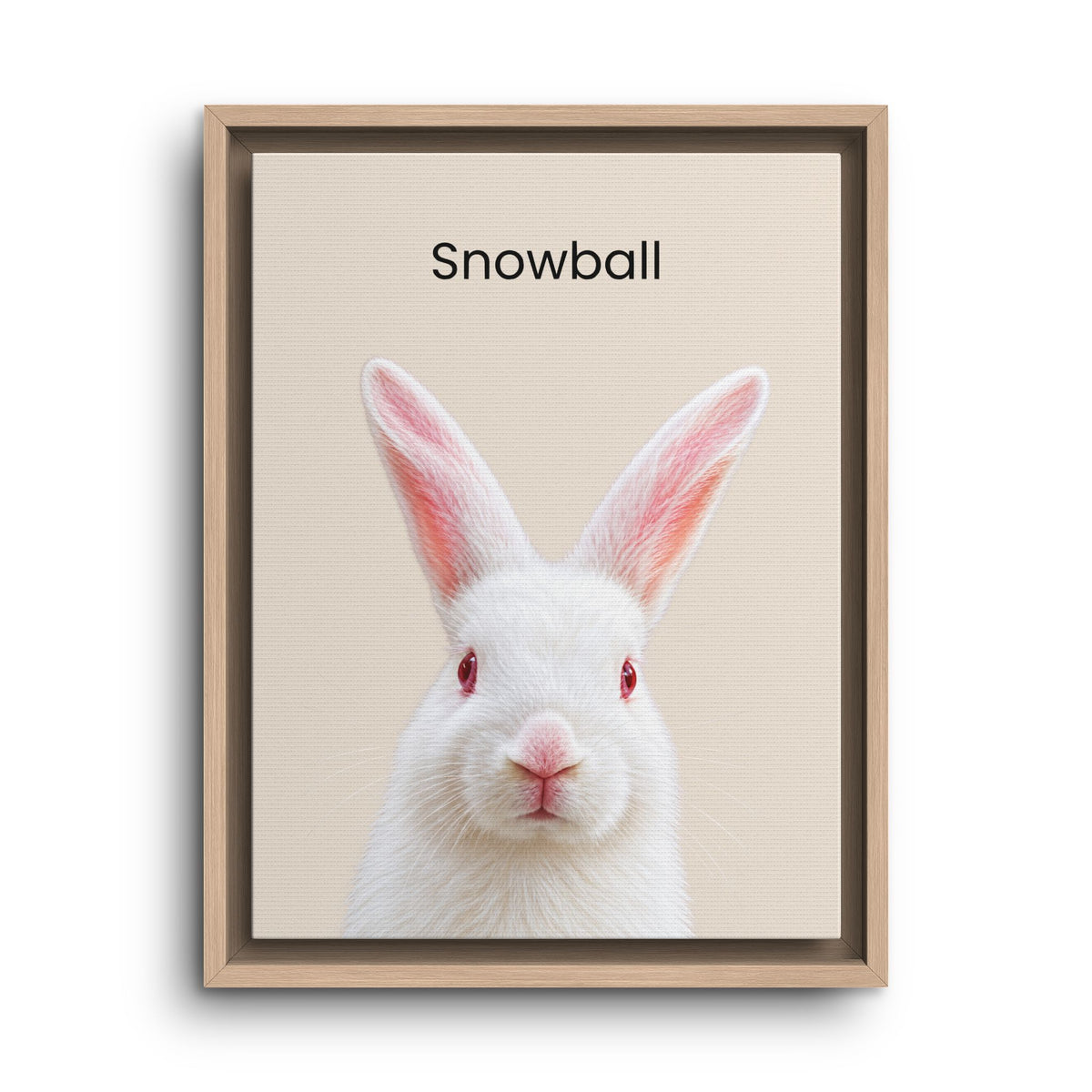 Framed wall art featuring a white rabbit centered on a light beige background with the word 'Snowball' printed above it. The piece is shown in a light wood frame against a white background.