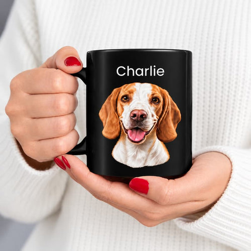 A person in a white ribbed sweater holds a black ceramic mug with a custom printed portrait of a beagle dog and the name 'Charlie' in white text. The person has red nail polish.